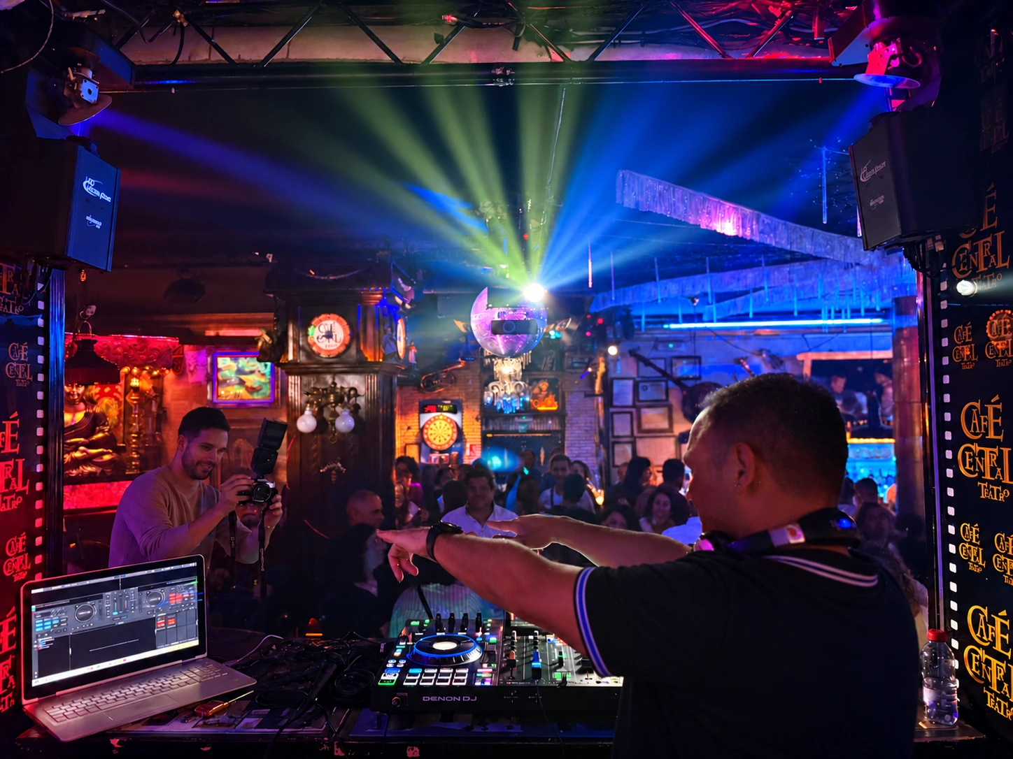 Achu DJ de perfil en la cabina, con ambos brazos extendidos señalando hacia la pista mientras un fotógrafo le captura en la sala Central